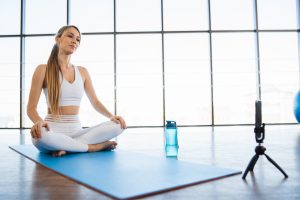 Female yoga trainer recording video lessons on smartphone in studio